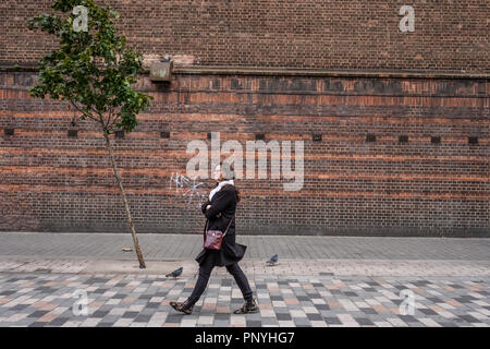 Eine einsame Person an einem einsamen Baum an einem windigen Tag in London. Stockfoto