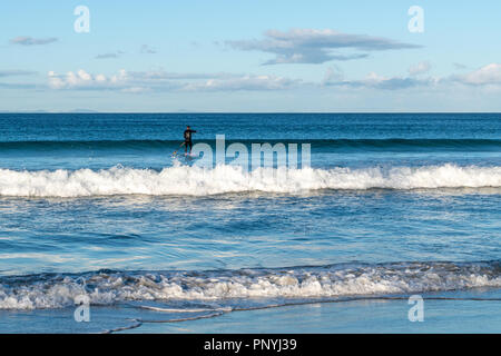 Single Surfer im Leerlauf auf den seichten Wellen mit einer blauen Meer Stockfoto