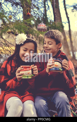 Zwei junge Kinder mit Tassen an Weihnachten Stockfoto