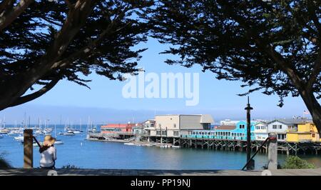 Frau mit breiten umrandet Hut sitzt auf Schritte mit Blick auf das historische alte Pier in Monterey, CA. Stockfoto
