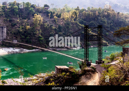 Rafting am Ganga Fluss während der Sommer in Rishikesh zusammen mit einem historischen Metallbrücke, ist der einzige Weg, um die Ganga Fluss zu überqueren. Stockfoto