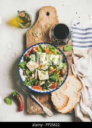 Flachbild-lay traditioneller Griechischer Salat mit Feta Käse, Olivenöl und Oliven und Glas Rotwein über Rustikal, das Board auf weißem Marmor Tabl Stockfoto