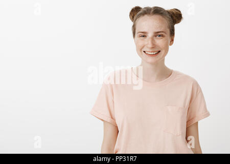 Mädchen liebt das Leben und die Freunde. Optimistisch sorglos feminine Frau im Rosa t-shirt mit Sommersprossen und niedlichen blauen Augen, freudig lächelnd an Kamera, während über grauer Hintergrund posiert, beiläufig im Gespräch Stockfoto