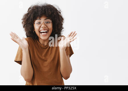 Taille-up Shot von überrascht verspielt und berührt gut aussehende Afrikanische amerikanische Frau in Gläser und stilvolle Braunes t-shirt Hände umklammern und lächelnd vor Freude und Aufregung mögen große Show Stockfoto