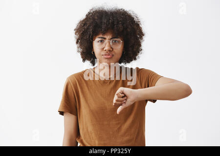 Mädchen verließ nach ruiniert Leistung enttäuscht. Portrait von unzufrieden und unbeeindruckt african american cute woman in Gläsern mit Afro Frisur mit Daumen nach unten und Schmollen aus Enttäuschung Stockfoto