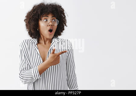 Taille-up Shot beeindruckt und begeistert afrikanische amerikanische Geschäftsfrau mit Afro Frisur in Gläsern und gestreifte Bluse keuchend auf der Suche und nach rechts mit Staunen und Interesse Stockfoto