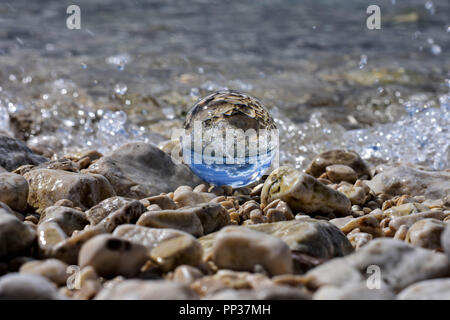 Glaskugel am felsigen Strand whit sea wave spiegeln sich darin sitzen/konzeptionellen Bild der Sommerferien Stockfoto