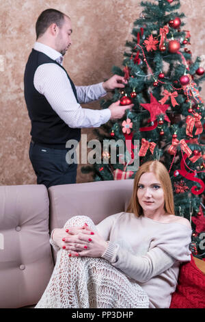 Mann ist hinter der Frau auf dem Sofa sitzen und schmücken den Weihnachtsbaum Stockfoto