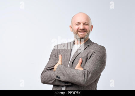 Reifen gut aussehender Mann in lässiger Anzug hält die Arme verschränkt und lächelnd, während gegen den weißen Hintergrund stehen. Stockfoto