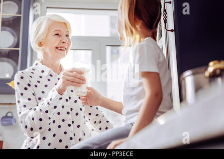 Heiter im Alter von Frau lächelnd, während Sie ein Glas Milch zu Kind Stockfoto
