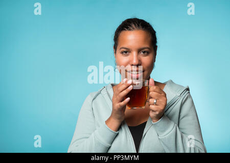 Schöne junge schwarze Frau trinken warmen Tee auf einem blauen Hintergrund Stockfoto