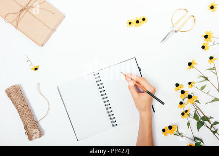 Frau, die Hinweise unter gelb Sommer Blumen und Geschenk, Ansicht von oben. Flach florale Komposition mit weibliche Hände schreiben in Tagebuch und Vorbereitung zur Holid Stockfoto