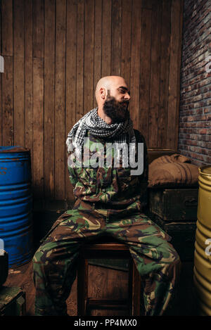 Captive Soldat sitzt auf einem Stuhl, Schrecken des Krieges gebunden. Terrorismus und Terror, militärischen Mann in khaki Camouflage, Barrel Kraftstoff oder Chemikalien auf Backgr Stockfoto