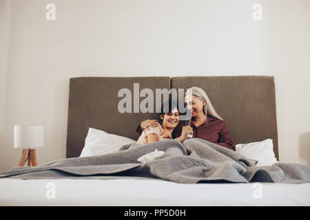 Ältere Frau mit ihrer Tochter auf dem Bett, zu Hause zu sitzen. Junge Frau verbringt Zeit mit ihrer alten Mutter. Stockfoto