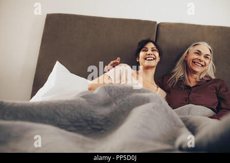Glückliche Tochter und Mutter liegend auf Bett zu Hause und gemeinsam lachen. Lächelnde Frau verbringt gerne Zeit mit ihrer Mutter lag auf dem Bett. Stockfoto