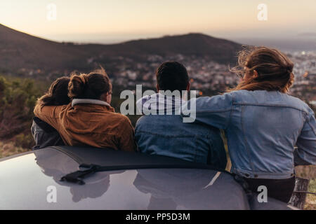 Ansicht der Rückseite zwei Paare stehen auf einer Autobahn. Eine Gruppe von Freunden auf einem Laufwerk Anhalten auf der Autobahn und Blick auf die Stadt von oben auf einem Hügel. Stockfoto