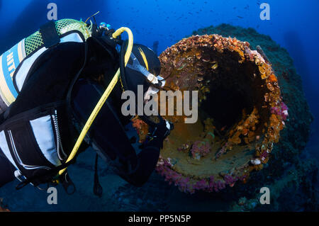 Weibliche Scuba Diver mit Taschenlampe erkundet das Innere eines großen Rohr mit Verkrusteten Meeresleben im La Plataforma Wrack (Formentera, Balearen, Spanien) Stockfoto