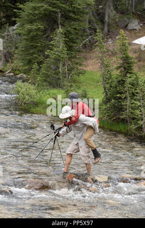 Mann, der Frau über einen Bach an einem Rucksack Reise in Oregon Wallowa Mountains. Stockfoto