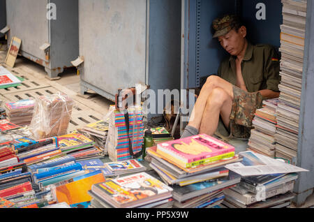 Chinesischer Mann arbeitet als Buchhändler Bücher verkaufen und warten auf Kunden an ein offenes Buch Markt in der Stadt Beijing, Kinn Stockfoto