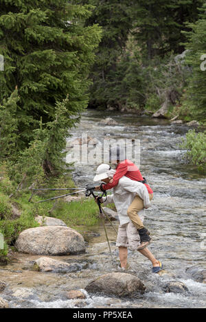 Mann, der Frau über einen Bach an einem Rucksack Reise in Oregon Wallowa Mountains. Stockfoto