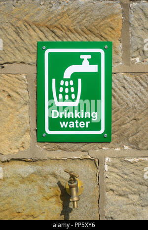 Eine grüne und weiße outdoor Trinkwasser Zeichen auf einer sandsteinmauer oberhalb einer Messing tippen Stockfoto