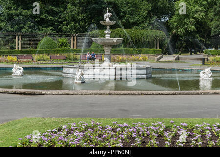 Die formale Brunnen in der Italienischen Gärten des Stanley Parks an einem sonnigen Sommertag, Blackpool Lancashire, England, Großbritannien mit zwei weit entfernte sitzen Menschen Stockfoto