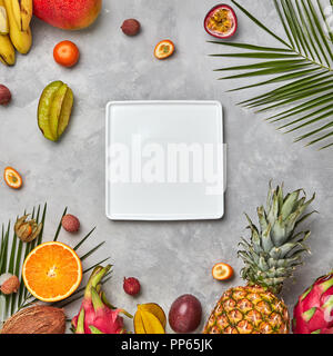 Quadratische weiße leere Platte nalmium Blätter und Früchte, saftig Trio kumkva, Physalis, Passionsfrucht, Banane auf grauem Beton Hintergrund mit kopieren. Die Zusammensetzung von Lebensmitteln. Flach Stockfoto