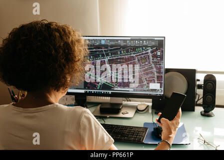 Architekt weiblichen Zeichnen mit CAD-Software entwerfen Gebäude. Ansicht von hinten. Sie hält ein Mobiltelefon Stockfoto