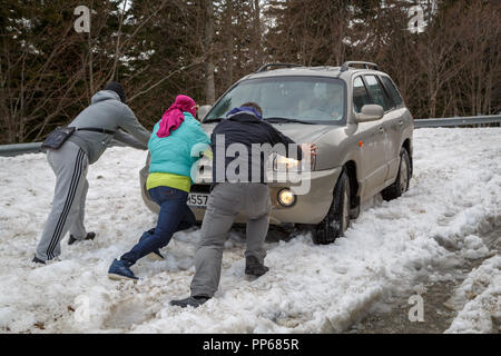 ADYGEA, Russland, 05. MAI 2015: Drei Leute drücken Sie ein Auto, das in tiefem Schnee blockiert ist. Stockfoto