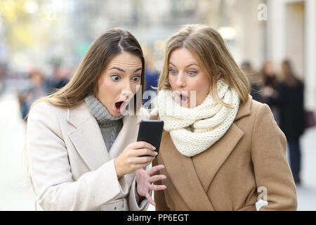 Vorderansicht Porträt von zwei überrascht Frauen lesen Telefon Inhalt im Winter auf der Straße Stockfoto