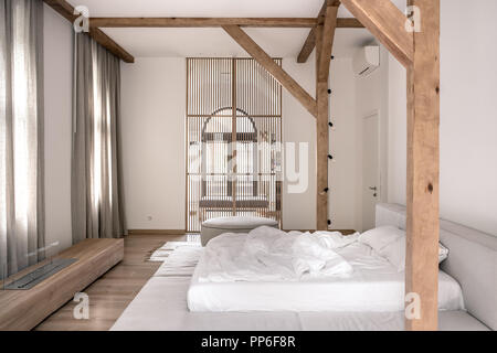 Modernes Schlafzimmer mit weißen Wänden, Parkettboden, Holzbalken und ein Gitter Partition. Es ist ein grauer Bett mit Bettwäsche, hängende Glühlampen, s Stockfoto