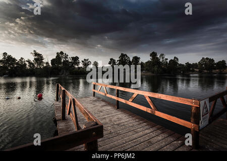 Pier mit hölzernen Balustrade vom Sonnenuntergang Sonne und Himmel mit Wolken bedeckt beleuchtet Stockfoto