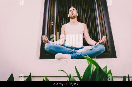 Junger Mann mit Yoga Körperhaltung namens Lotus Blume im Fenster Stockfoto