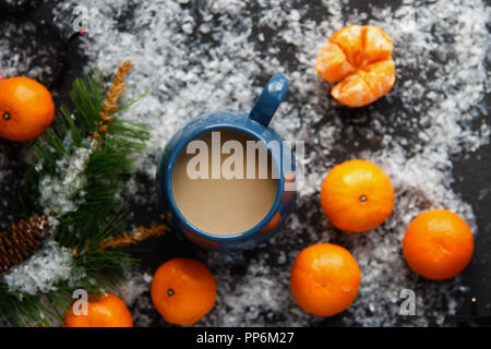 Weihnachten und Neujahr Konzept. Mandarinen, Kaffeebecher, Schnee, Weihnachten Baumstrukturzweig. Vor einem dunklen Hintergrund. Flach Top View Stockfoto