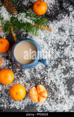 Weihnachten und Neujahr Konzept. Mandarinen, Kaffeebecher, Schnee, Weihnachten Baumstrukturzweig. Vor einem dunklen Hintergrund. Flach Top View Stockfoto