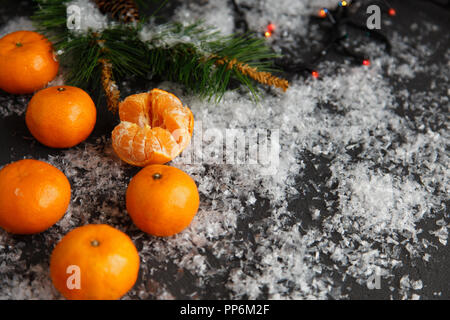 Weihnachten und Neujahr Konzept. Mandarinen, Kaffeebecher, Schnee, Weihnachten Baumstrukturzweig. Vor einem dunklen Hintergrund. Flach Top View Stockfoto