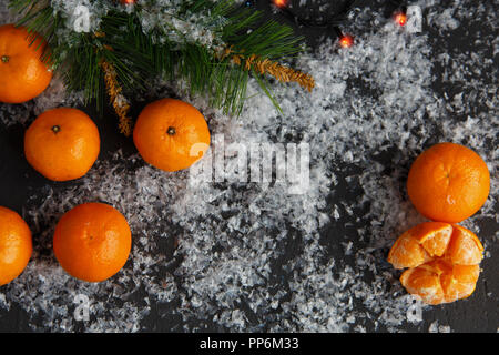 Weihnachten und Neujahr Konzept. Mandarinen, Kaffeebecher, Schnee, Weihnachten Baumstrukturzweig. Vor einem dunklen Hintergrund. Flach Top View Stockfoto