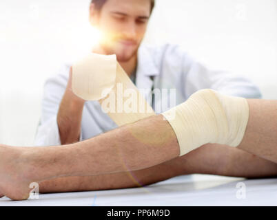 Arzt bandagieren eine Wunde am Bein des Patienten Stockfoto