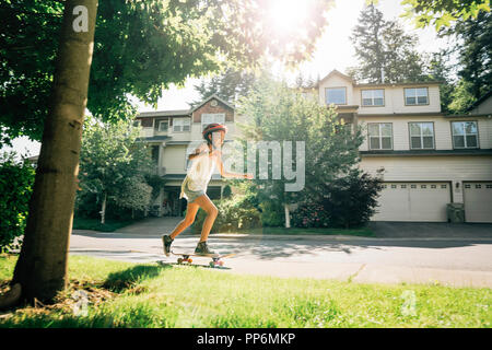 Tween Girl Schlittschuhlaufen auf Skateboard auf Bürgersteig in Wohngegend Stockfoto