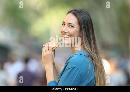 Glückliche Frau essen einen Burger in Kamera schaut auf der Straße Stockfoto