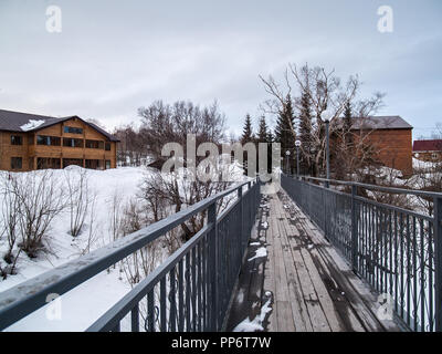 Die Straße auf einer hölzernen Brücke mit Metallschienen, die verschneite Häuser im Winter in der Dämmerung am Abend Stockfoto