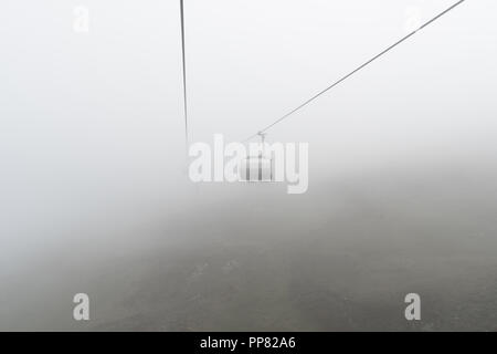 Leere Sessellift und Kabel in einem trüben und nebligen Berglandschaft im frühen Herbst in einem Skigebiet in der Schweiz Stockfoto