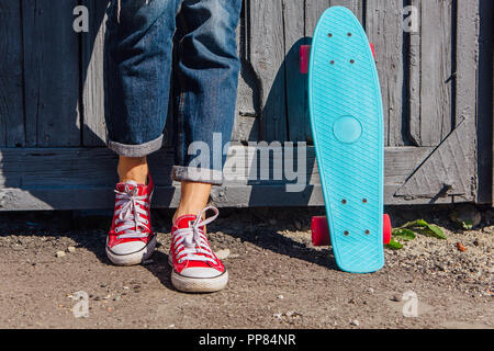 Close up Füße eines Mädchens in rote Turnschuhe und Blue Penny Skate Board mit rosa Räder neben der Wand stehen. Städtische Szene, Leben in der Stadt. Sport, Fitness Stockfoto