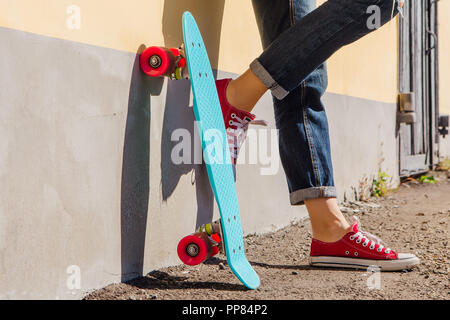 Close up Füße eines Mädchens in rote Turnschuhe und Blue Penny Skate Board mit rosa Räder neben der Wand stehen. Städtische Szene, Leben in der Stadt. Sport, Fitness Stockfoto