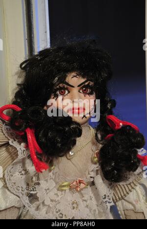 Eine Nahaufnahme eines antiken Porzellanpuppe mit langen schwarzen Haaren und einem unheimlich, schönes Gesicht, mit Narben; in einer weißen vintage Kleid, Halloween Stockfoto