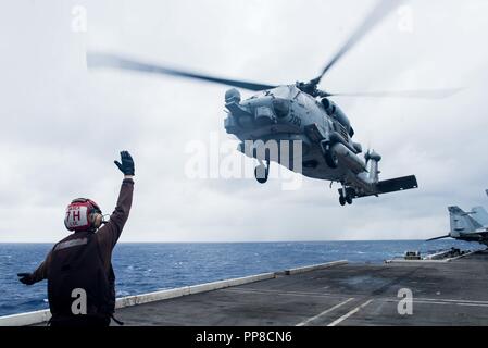 180920-N-OY 799-0047 philippinischen Meer (September 20, 2018) ein Matrose zu Hubschrauber Maritime Strike Squadron (HSM) 77 zugeordnet leitet eine MH-60R Sea Hawk, wie es von der Flight Deck der Marine vorwärts startet bereitgestellten Flugzeugträger USS Ronald Reagan (CVN 76) Während der Valiant Shield 2018. Das zweijährige, nur in den USA, Ausbildung Übung konzentriert sich auf die Integration der gemeinsamen Ausbildung von der US Navy, Air Force und Marine Corps. Dies ist der siebte Übung in der Valiant Shield-Serie, die 2006 begann. (U.S. Marine Foto von Mass Communication Specialist 2. Klasse Kenneth Abbate) Stockfoto