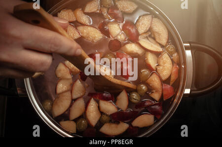 Mitreißend bunte Apfelscheiben, Obst Mix in einem Topf mit Löffel aus Holz. Erfrischende Frucht Apfelwein Punsch Party Trinken. Warme Glühen. Stockfoto