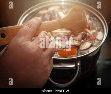 Mitreißend bunte Apfelscheiben, Obst Mix in einem Topf mit Löffel aus Holz. Erfrischende Frucht Apfelwein Punsch Party Trinken. Warme Glühen. Stockfoto