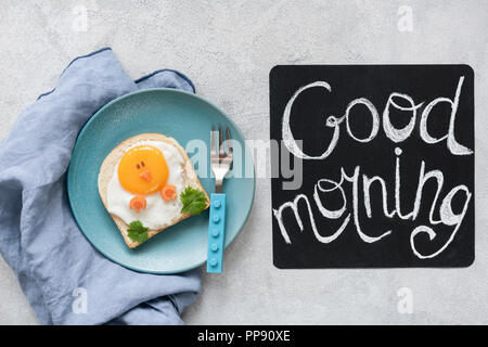 Frühstück Kinder. Lustige Toast mit Ei und guten Morgen Text auf einem schwarzen Brett. Ansicht von oben Stockfoto