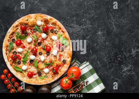Leckere Pizza auf Schwarz konkreten Hintergrund, Ansicht von oben kopieren und Platz für Text. Italienische Pizza mit Tomaten, Mozzarella, schwarzen Oliven und Rucola Stockfoto